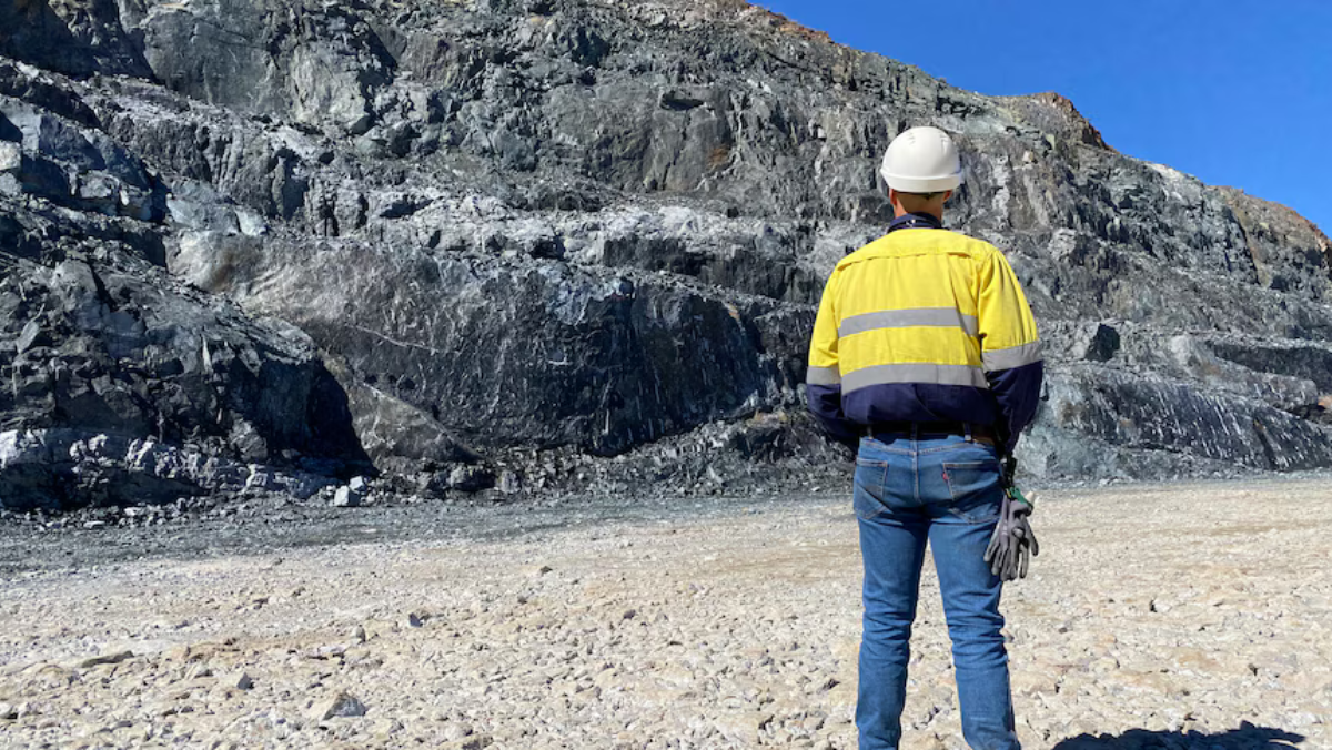 Mining worker in high-visibility gear surveying rock face at open-pit mine
